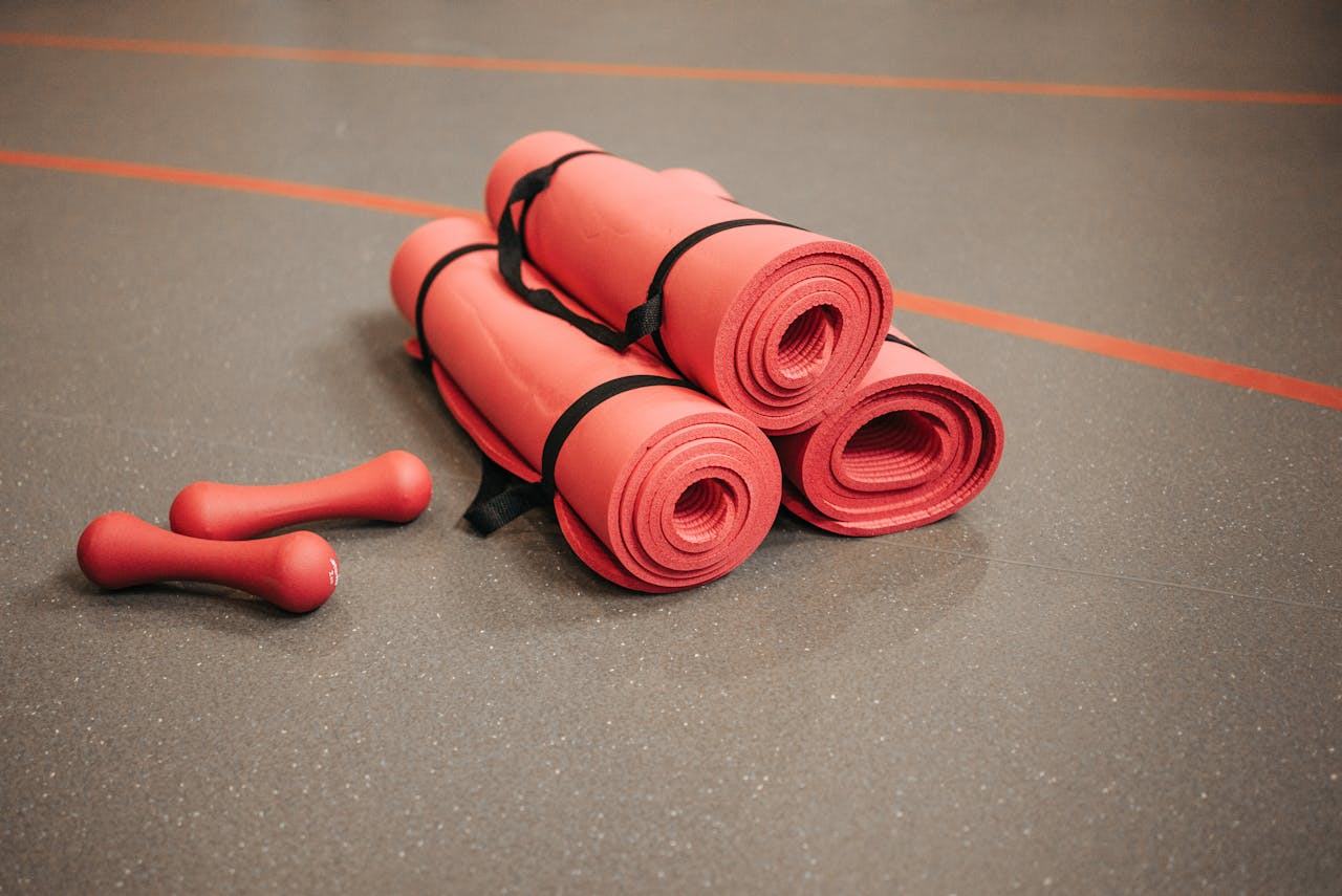 Red exercise mats and dumbbells on a gym floor, perfect for home or studio fitness.