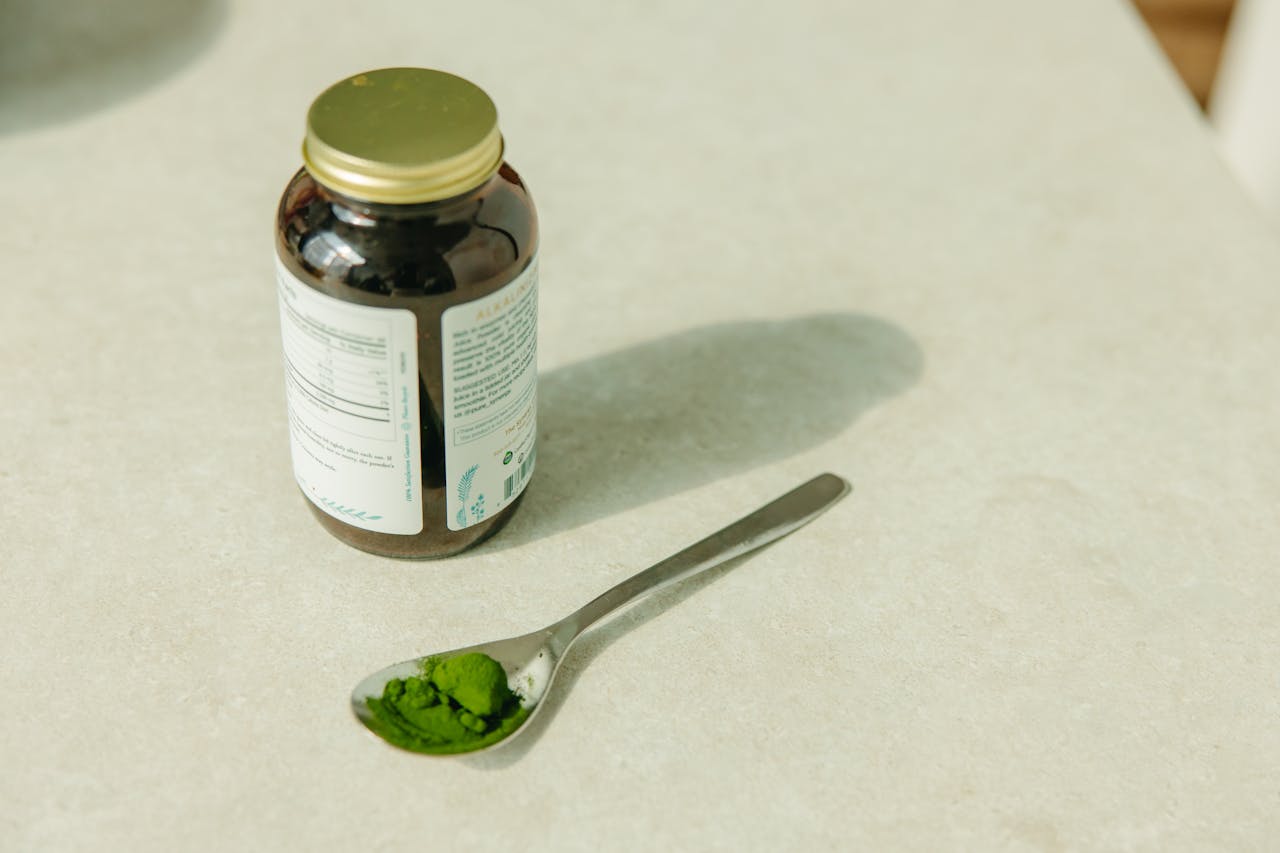 about-02 Close-up of a jar and a spoon with green powder, ideal for healthcare and wellness themes.
